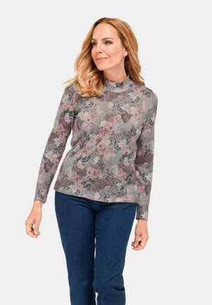 Langarmoberteil aus einem weichen Stoff, mit einem grau-pinken Blumenmuster, einem hohen Kragen und lockerer Passform. Kombiniert mit dunklen Denim-Jeans.