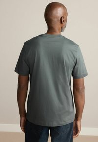 Tricou scurt cu mânecă scurtă, de culoare gri închis, cu gât rotund, realizat dintr-un material neted, având un croi lejer și detalii minime.