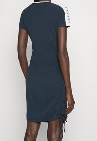 Laivan sininen mekko lyhyillä hihoilla, jossa on valkoisia yksityiskohtia hartioissa, sivuilla rypytystä ja pehmeää, teksturoitua kangasta.