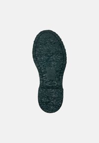 Grön gummiskosula med texturerade ytmönster, en central logotyp och konturer för grepp. Övergripande oval form med tydliga kanter.