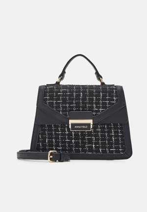 Sac à main en tweed noir et blanc avec un design structuré et des accents dorés. Il comprend une poignée supérieure et une bandoulière amovible.