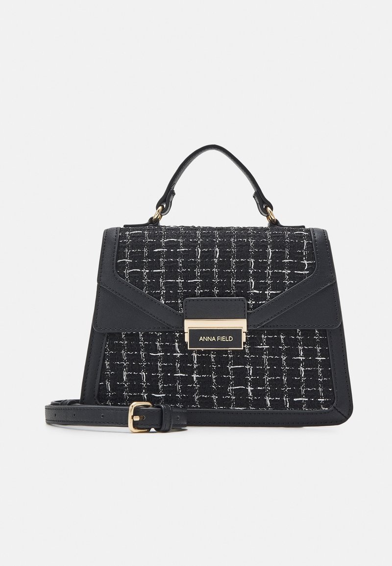 Sac à main en tweed noir et blanc avec un design structuré et des accents dorés. Il comprend une poignée supérieure et une bandoulière amovible.