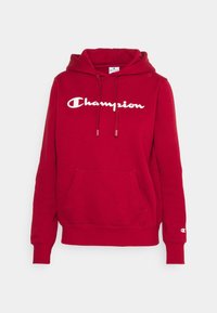 Červená bavlněná mikina s kapucí a šňůrkou, přední kapsa a bílé logo "Champion". Má žebrované manžety a spodek, měkkou texturu.