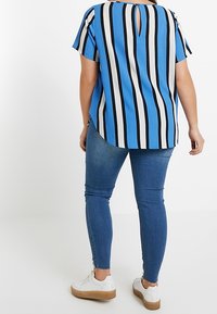 Modro-bílý pruhovaný krátký rukáv top s detailem ve tvaru klíčové dírky na zádech, spárovaný se slim-fit džíny a bílými teniskami s khaki podrážkou.