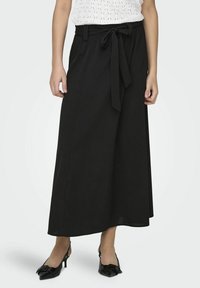 Jupe maxi noire en tissu léger. Caractérisée par une taille à nouer, des jambes larges et une texture douce, stylisée avec des talons slingback noirs.