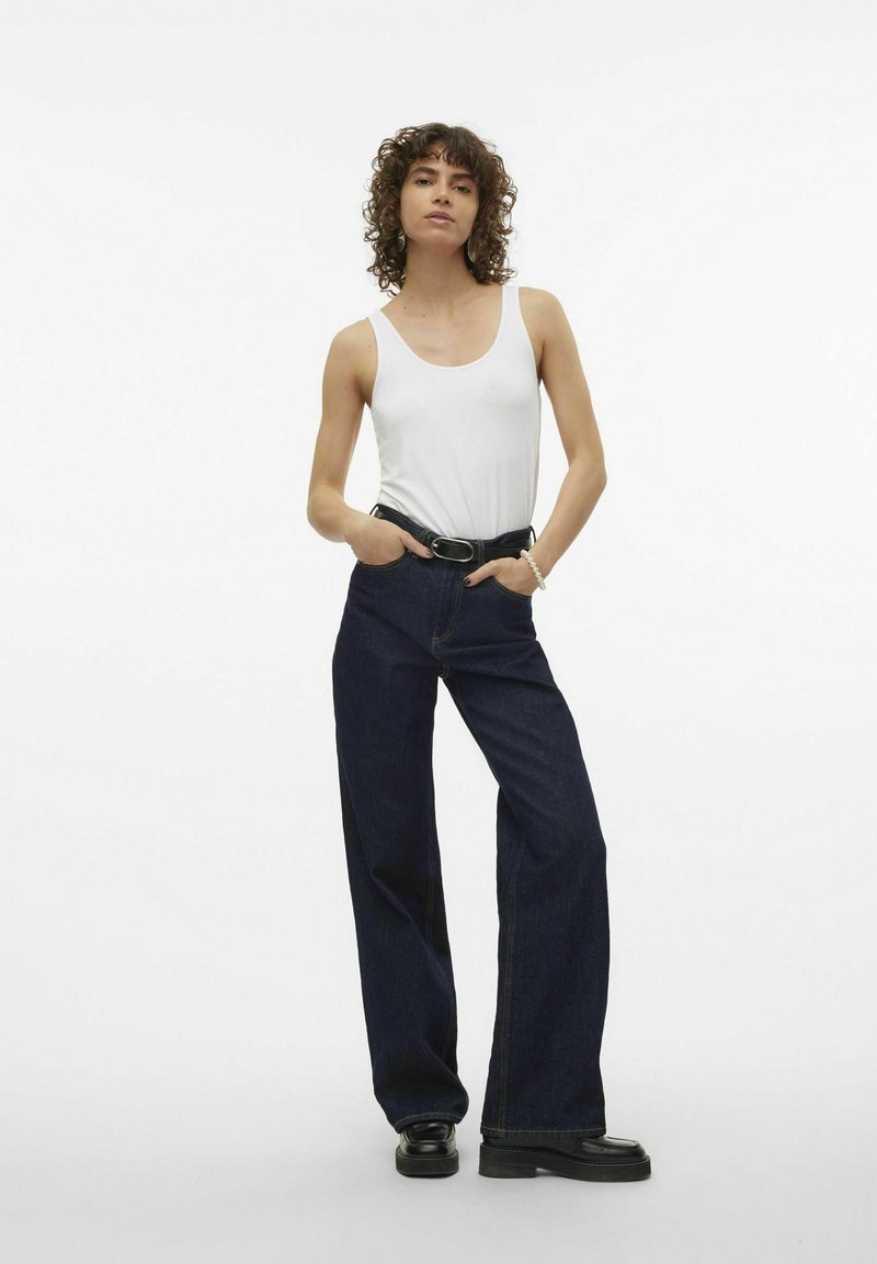 Wijduitlopende donkerdenim jeans met een hoge taille, gecombineerd met een strakke witte tanktop. Accentueert met een zwarte riem en robuuste zwarte schoenen.