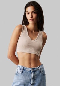 Top corto de canalé beige con escote en V y tirantes gruesos, combinado con vaqueros de denim azul claro. El top es ajustado y texturizado.