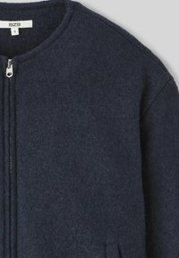 Veste bleu marine en mélange de laine avec un col rond et une fermeture éclair pleine longueur, dotée de deux poches latérales et d'une surface texturée.