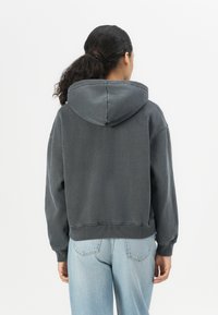 Gray cropped hoodie with a spacious hood, ribbed cuffs, and hem. Made from soft fabric, displayed with light blue jeans in a neutral background.