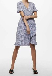 Lila Blumenwickelkleid mit kurzen Ärmeln, rüschigem Saum und einem Bindeband in der Taille. Der Stoff zeigt kleine, mehrfarbige Muster.