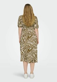 Bruine en crèmekleurige zebraprint jurk met korte pofmouwen en een gerimpelde zoom, gecombineerd met witte sneakers. Zacht materiaal en een relaxte pasvorm.
