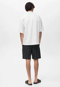 Witte korte mouwen shirt, zwarte gestreepte shorts en zwarte sandalen. Het shirt heeft een rechte snit; de shorts hebben voorzakken en een tailleband.