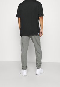 Šedé tepláky s elastickými manžetami a malým barevným logem; v kombinaci s černým tričkem s krátkým rukávem. Bílá sportovní obuv dokončuje vzhled.