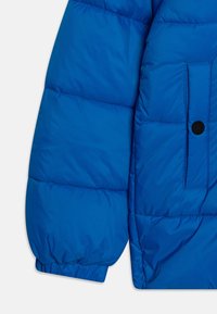Modrá péřová bunda s prošívanými sekcemi, elastickými manžetami a kapsou na knoflík. Vyrobena z lehkého, voděodolného materiálu.