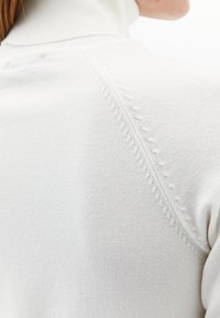 Witte gebreide turtleneck trui met een geribde kraag, een soepele textuur en contrasterende stiksels langs de schoudernaad.