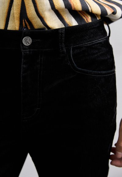 Melni denim džinsi ar gludu, gludu tekstūru, ar priekšējo kabatu un metāla pogas detaļu jostasvieta.
