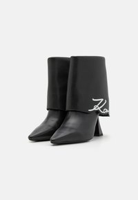 Black leather ankle boots with pointed toes, a unique fold-over design at the top, and a white script logo accent on the side.