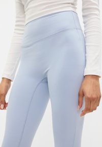 Leggings alta vita blu chiaro realizzati in materiale elasticizzato con una superficie liscia. Presentano cuciture piatte e una silhouette aderente.