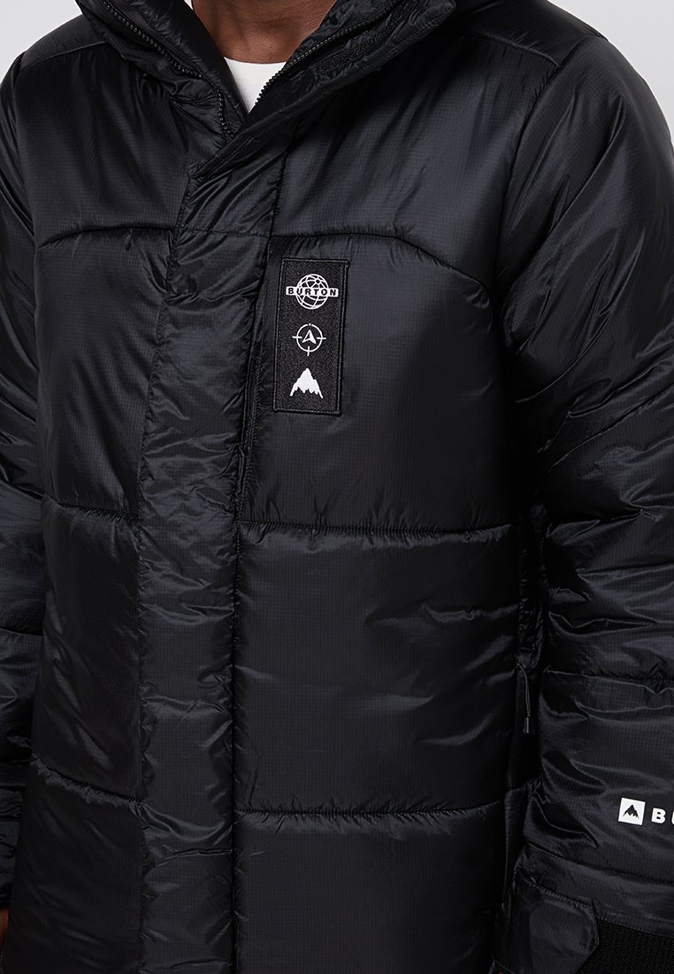 Schwarze Steppjacke mit Reißverschluss, ausgestattet mit einer Kapuze, strukturiertem Stoff, vertikaler Naht und einem Logo-Patch auf der Brust.