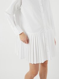 Robe blanche à boutonnière sur le devant, manches longues et jupe plissée. Le tissu semble lisse avec un design structuré.
