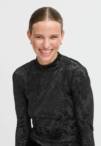 Top nero a maniche lunghe con collo alto, caratterizzato da una texture floreale in velluto. Il tessuto appare morbido, con una leggera lucentezza e un design aderente.