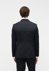 Casaco de fato azul-marinho com um corte ajustado, tecido suave, gola com notches e punhos abotoados, exibindo uma vista traseira limpa e minimalista.