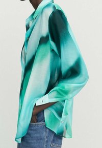 Chemise ample à boutons, en dégradé de vert et de bleu, réalisée dans un tissu léger à la texture douce. Manches longues et col pointu.