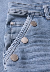 Pantalones cortos de mezclilla de color azul claro con un diseño de cierre de botón y cinco botones de metal. Los detalles de costura realzan la textura de la tela.