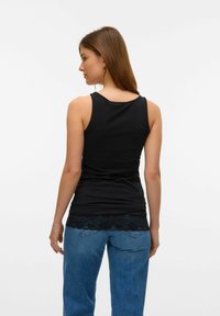 Schwarzes ärmelloses Tanktop mit einer Spitzenborte am Saum, kombiniert mit blauen hochtaillierten Jeans im lockeren Schnitt und lässigen Design.