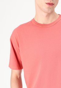 Kortsleeve korall t-skjorte med rund hals, laget av mykt stoff. Den har kontrastsøm langs halslinningen og ermene.