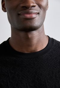 Sort sweatshirt med struktur, der har en ribbet rund halsudskæring, og subtile geometriske mønstre, der skaber visuel interesse og dybde.