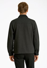 Mörkgrå langärmad skjorta med kragdesign, knäppta ärmslut, rak nederkant och textilstruktur. Bakvy visar sömmar.