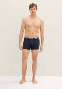 Tengerés kék pamut boxer nadrág márkás elasztikus derékpánttal. Sima textúra és testhezálló kialakítás, férfi modellen bemutatva.