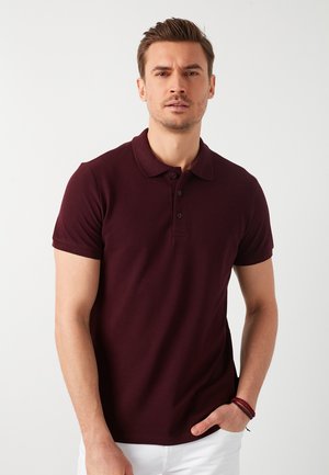 Bordeaux polo med en blød tekstur, korte ærmer og en tre-knaps lukning. Har en klassisk krave og en tætsiddende pasform.