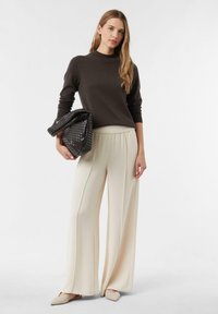 Brauner Strickpullover mit langen Ärmeln, cremefarbeneweit geschnittene Hose mit elastischem Bund und einer strukturierten schwarzen Tasche. Neutrale flache Schuhe.