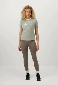 Šviesiai žalia marškinėliai su baltu spaudiniu, derinami su rudomis leggingais. Marškiniai turi apvalų iškirpimą ir trumpas rankoves, pagaminti iš medvilnės.