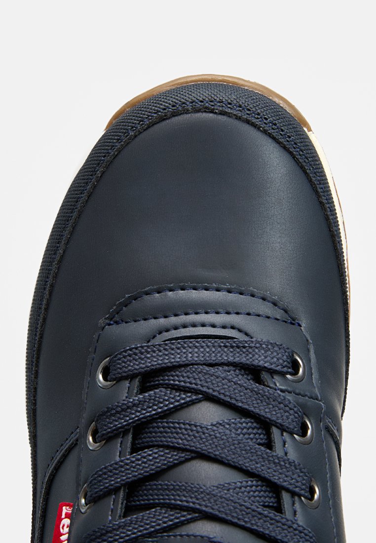 Baskets bleu marine avec une tige en cuir lisse, des accents en tissu texturé, des lacets ronds et une semelle en caoutchouc. Présente un logo rouge sur le côté.