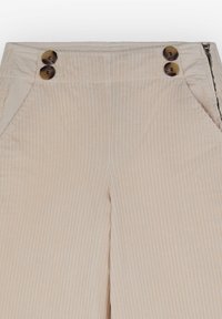 Pantalon beige en velours côtelé avec des côtes verticales, doté de deux boutons marron de chaque côté près de la taille et de poches latérales.