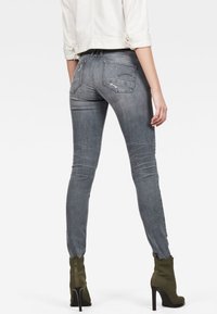 Jeans ajustados de denim gris con detalles desgastados, cuatro bolsillos y un diseño entallado. Combinados con botas de tobillo verdes oliva y una chaqueta corta blanca.