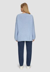 Hellblaues, übergroßes Strickpullover mit einem strukturierten Muster, ausgestattet mit einem weiten Ausschnitt und einem gerippten unteren Saum, kombiniert mit dunkelblauen Hosen.