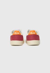 Sko med hvit skinnkropp, burgunder semsket hæl og oransje hælgrep med "VEJA"-logo. Kremfarget gummisåle. Minimalistisk design.