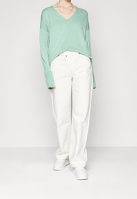 Mintgrön V-ringad tröja med droppade axlar, matchad med löst sittande vita denimjeans och vita sneakers.