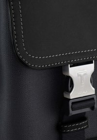 Borsa in materiale nero texturizzato con un pattina grigia cucita e chiusura in metallo argentato. Presenta una tracolla con hardware regolabile.