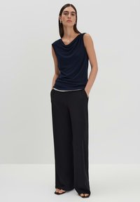 Top senza maniche di colore blu navy con collo a cowl, abbinato a pantaloni larghi neri. Il tessuto ha una texture liscia e una vestibilità morbida.