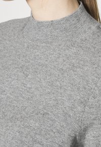 Pull en maille grise avec un col montant côtelé, présentant une texture douce et une finition lisse, mettant en avant un design simple et minimaliste.