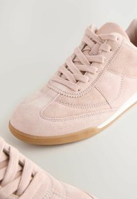 Baskets en suède rose clair avec une texture lisse, devant lacé, détails de couture sur le côté et une semelle en caoutchouc brun.