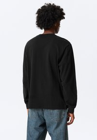 Musta pitkähihainen t-paita, jossa pyöreä pääntie, rento istuvuus ja pehmeä puuvillamateriaali, yhdistetty vaaleanpesuisiin farkkuihin.