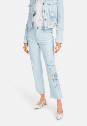 Light blue denim jacket and matching pants, featuring floral embroidery in pastel colors. White pointed flats complete the outfit.