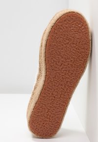Espadrille sål med en struktureret brun gummibase, juteindpakning og en glat øverste kant. Lysfarvet stof synligt øverst.