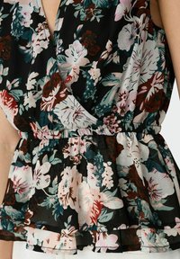 Top envolvente floral con fondo negro y flores en tonos rosa, blanco y verde azulado. Detalle de dobladillo con volantes y cintura elástica. Tela ligera.